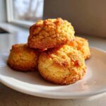 A close-up of four golden brown 3-ingredient butter cookies stacked on a white plate near a window.
