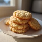 A stack of golden, crumbly 3-ingredient butter cookies resting on a white plate near a window.