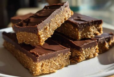 A stack of homemade, no-bake protein bars with a thick layer of chocolate topping resting on a white plate.