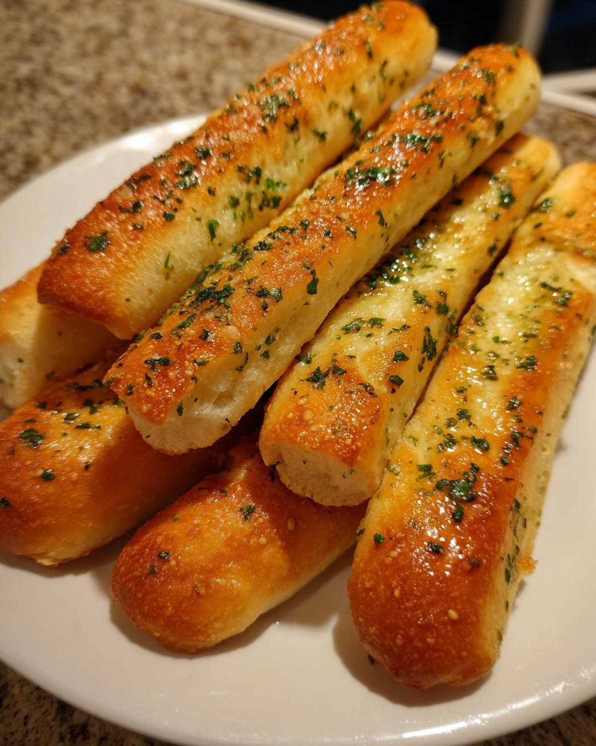 A stack of freshly baked, golden brown breadsticks brushed with garlic butter and sprinkled with parsley.