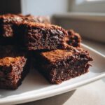 Close-up of several rich, dark chocolate squares of 3 ingredient fudge stacked on a white plate.