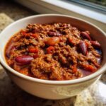 Close-up of a creamy white bowl filled with rich, hearty chili featuring ground meat and kidney beans.