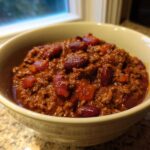A close-up of a creamy bowl filled with rich, meaty chili and kidney beans.