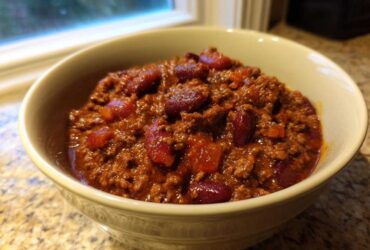 A close-up of a creamy bowl filled with rich, meaty chili and kidney beans.