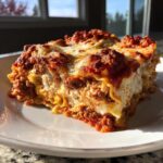 A thick, multi-layered slice of homemade lasagna with rich meat sauce and melted cheese, served on a white plate.