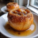 A close-up of a perfectly baked apple topped with cinnamon sugar and sitting in sweet syrup.