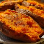 Close-up of fluffy, bright orange baked sweet potatoes split open and seasoned with pepper.