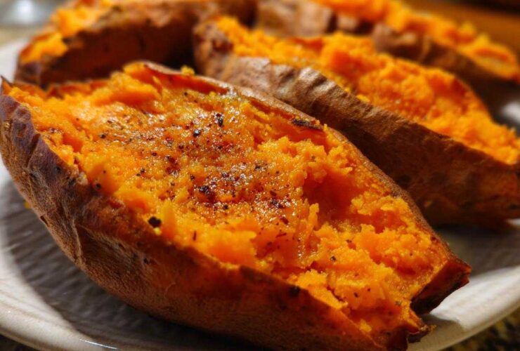 Close-up of fluffy, bright orange baked sweet potatoes split open and seasoned with pepper.