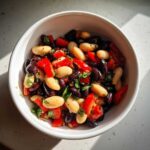 A close-up overhead shot of a vibrant bean salad featuring black beans, white beans, and diced red peppers.