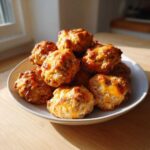 A white bowl stacked high with golden brown, cheesy bisquick sausage balls, lit by natural sunlight.