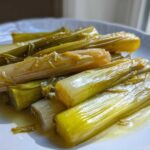 Close-up of tender, glistening braised leeks served on a white plate with a light sauce.