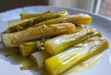 Close-up of tender, glistening braised leeks served on a white plate with a light sauce.