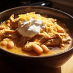 A close-up of a hearty bowl of white chicken chili topped with shredded cheese and sour cream.