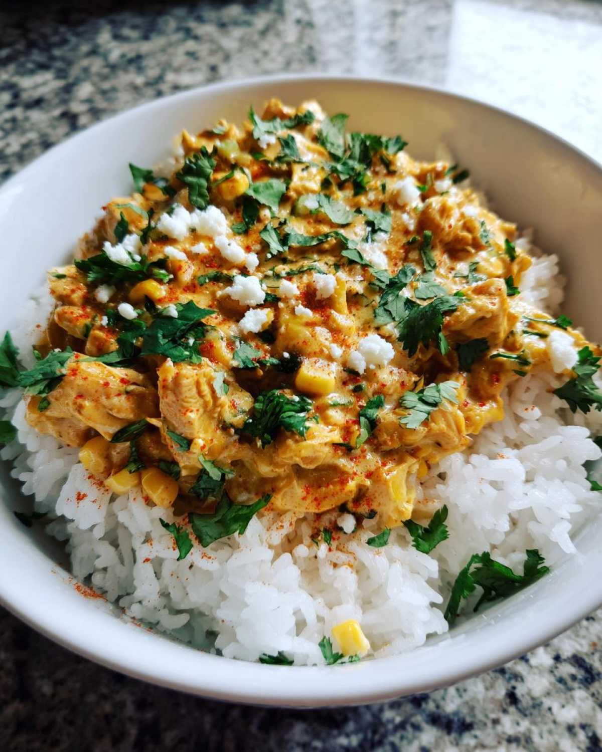 Close-up of a creamy, orange-sauced chicken rice bowl topped with cotija cheese and fresh cilantro.