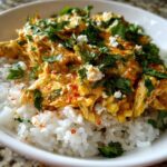 Close-up of a delicious chicken rice bowl featuring shredded chicken in a creamy orange sauce over white rice, topped with cilantro and cheese.