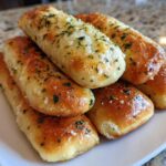 A stack of freshly baked, golden brown breadsticks brushed with garlic butter and sprinkled with parsley.