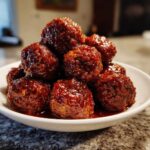 A mound of glossy, sauce-covered cranberry meatballs piled high in a small white serving bowl.