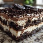 A close-up slice of layered dirt cake featuring cream, chocolate mousse, and crushed Oreos, topped with whole Oreos.