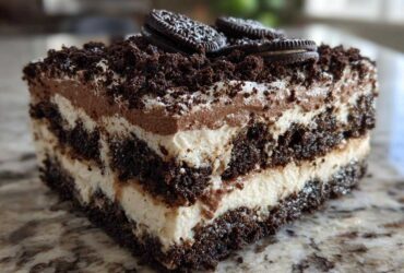 A close-up slice of layered dirt cake featuring cream, chocolate mousse, and crushed Oreos, topped with whole Oreos.