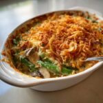 A close-up of a freshly baked green bean casserole topped with crispy fried onions, showing creamy sauce and mushrooms.