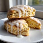 Close-up of two stacked, glazed lemon scones on a white plate, showing the thick, dripping icing.