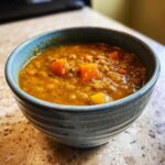 Close-up of a rustic blue bowl filled with thick, orange-hued lentil soup featuring visible chunks of carrots.