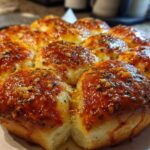 Close-up of freshly baked, gooey pizza sliders topped with a shiny garlic butter glaze and herbs.