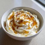 A white bowl filled with creamy whipped ricotta dip, drizzled generously with golden honey and spices.