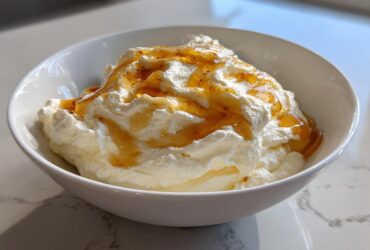 A white bowl filled with fluffy ricotta dip topped generously with golden honey.