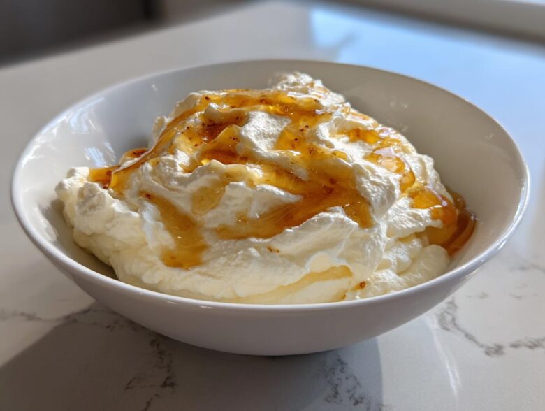 A white bowl filled with fluffy ricotta dip topped generously with golden honey.