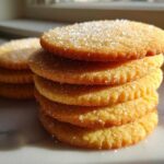 Close-up of a tall stack of golden brown sugar cookies topped with coarse sparkling sugar.