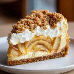 Close-up of a decadent slice of apple pie cheesecake topped with whipped cream and streusel crumble.