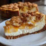 A close-up slice of apple pie cheesecake featuring a graham cracker crust, creamy filling, apple topping, and streusel crumble.