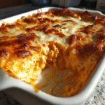 Close-up of hot, baked buffalo chicken dip in a white casserole dish with a scoop already taken out.