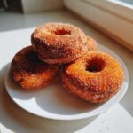 A stack of four golden brown baked pumpkin donuts generously coated in cinnamon sugar, resting on a white plate.