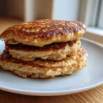 A stack of three golden-brown banana oatmeal pancakes served on a white plate.