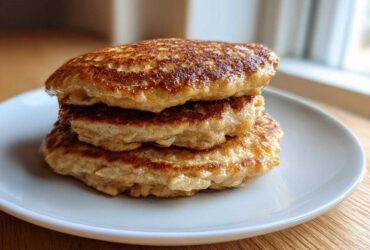 A stack of three golden-brown banana oatmeal pancakes served on a white plate.