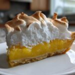Close-up of a perfect slice of lemon meringue pie showing bright yellow filling and toasted meringue.