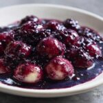Close-up of plump, round Blackberry Dumplings soaking in a rich, dark purple blackberry sauce.