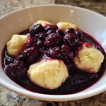 Close-up of warm Blackberry Dumplings served in a white bowl, covered in rich, dark blackberry sauce.