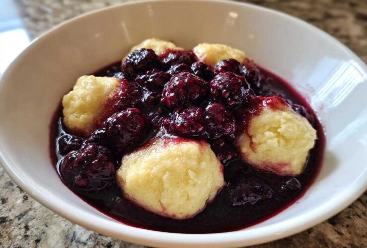 Close-up of warm Blackberry Dumplings served in a white bowl, covered in rich, dark blackberry sauce.