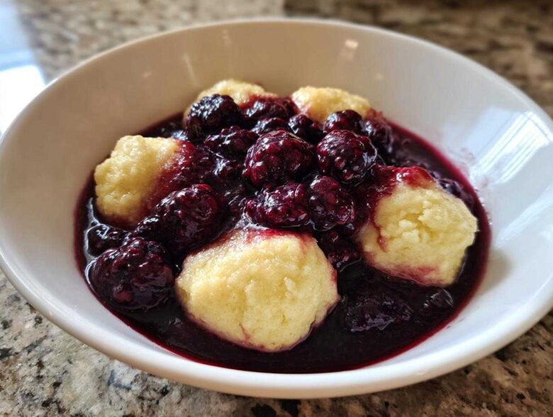 Close-up of warm Blackberry Dumplings served in a white bowl, covered in rich, dark blackberry sauce.