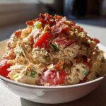 A close-up of creamy blt chicken salad mixed with tomatoes and topped generously with crispy bacon bits in a white bowl.