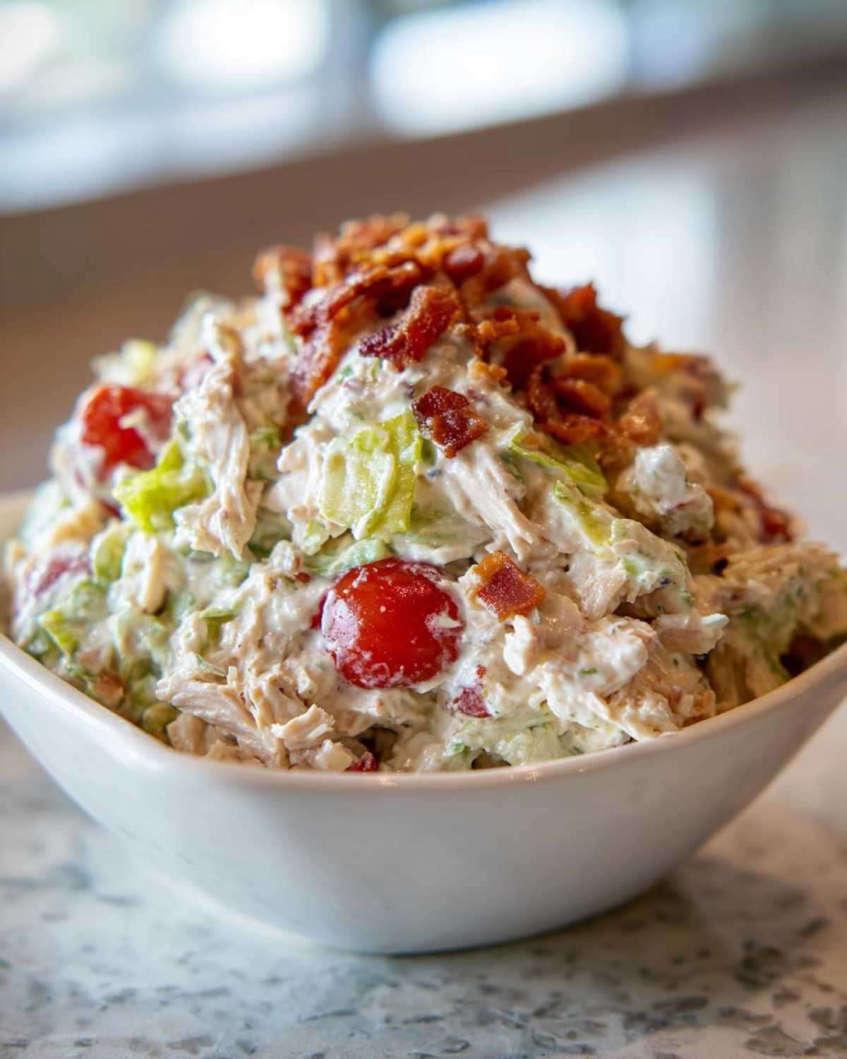 A close-up of a generous serving of creamy blt chicken salad, featuring shredded chicken, lettuce, cherry tomatoes, and topped with crispy bacon.