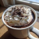 Close-up of a rich boozy hot chocolate topped with whipped cream and chocolate shavings in a white mug.