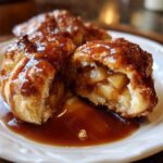 Close-up of a warm apple dumpling cut in half, showing spiced apple filling and drizzled with caramel sauce.