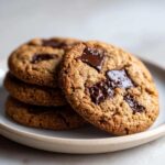 Close-up of a stack of four delicious vegan chocolate chip cookies with melted dark chocolate chunks.