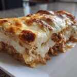 A generous slice of rich chicken alfredo lasagna showing layers of shredded chicken and creamy sauce topped with bubbly, browned cheese.