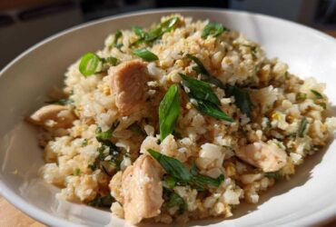 Close-up of a white bowl filled with chicken cauliflower fried rice topped with fresh green onions.