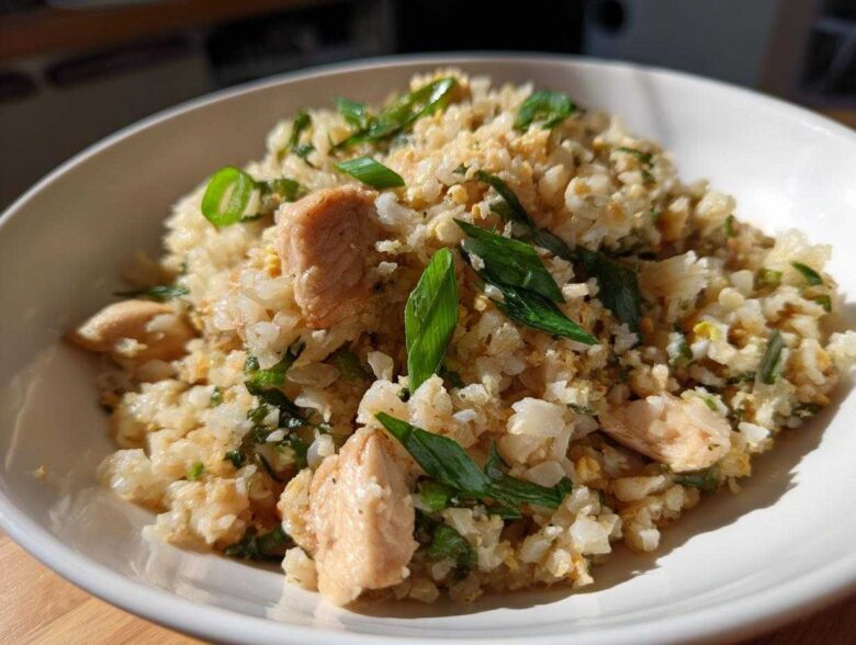 Close-up of a white bowl filled with chicken cauliflower fried rice topped with fresh green onions.
